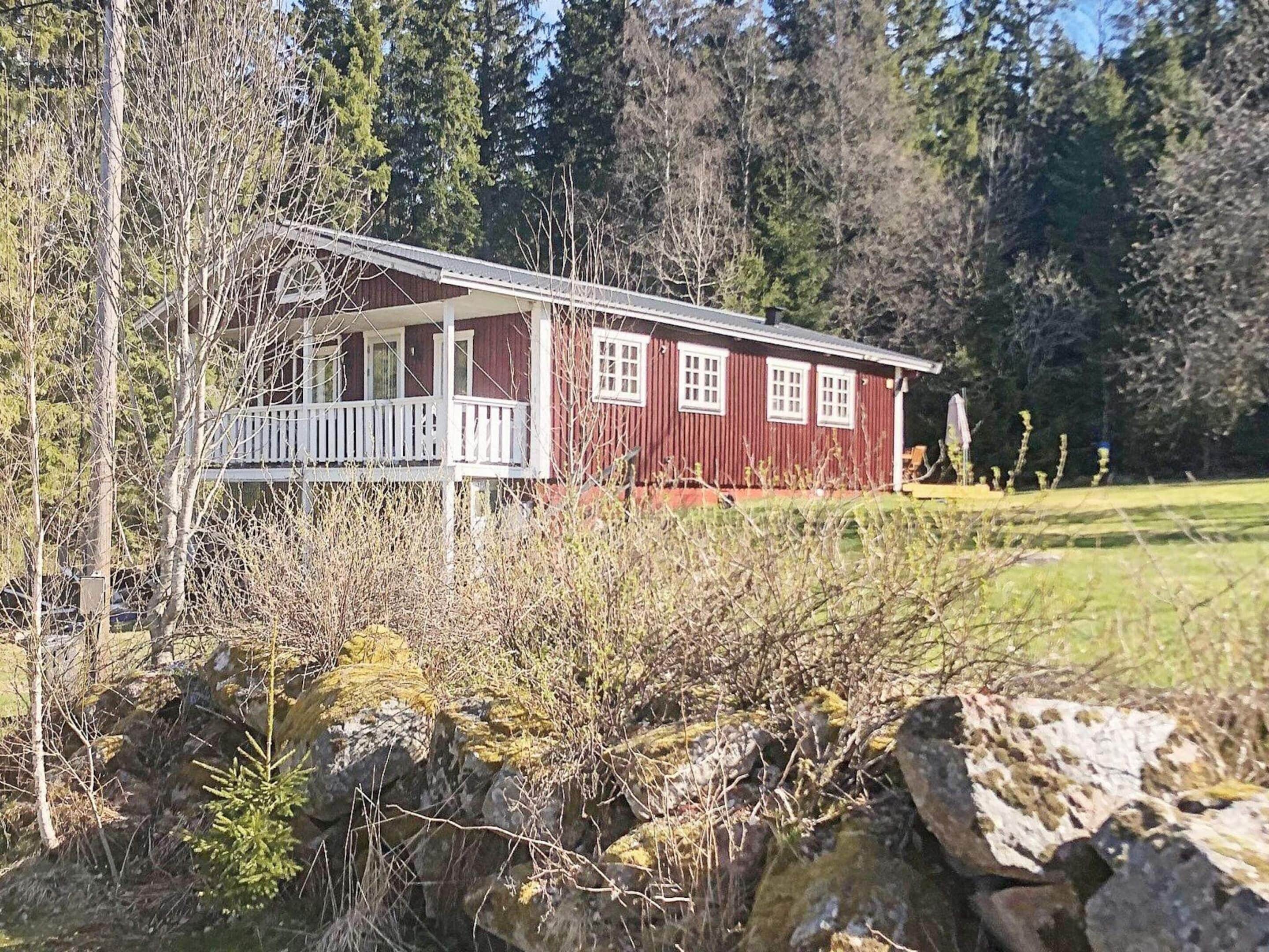 A red cabin with a porch and a small deck, surrounded by trees and a grassy area.