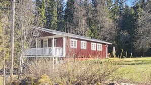 A red cabin with a porch and a small deck, surrounded by trees and a grassy area. - 6 Person Holiday Home in Savsjo (Savsjo)