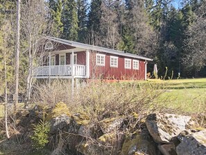 A red cabin with a porch and a small deck, surrounded by trees and a grassy area. - 6 Person Holiday Home in Savsjo (Savsjo)