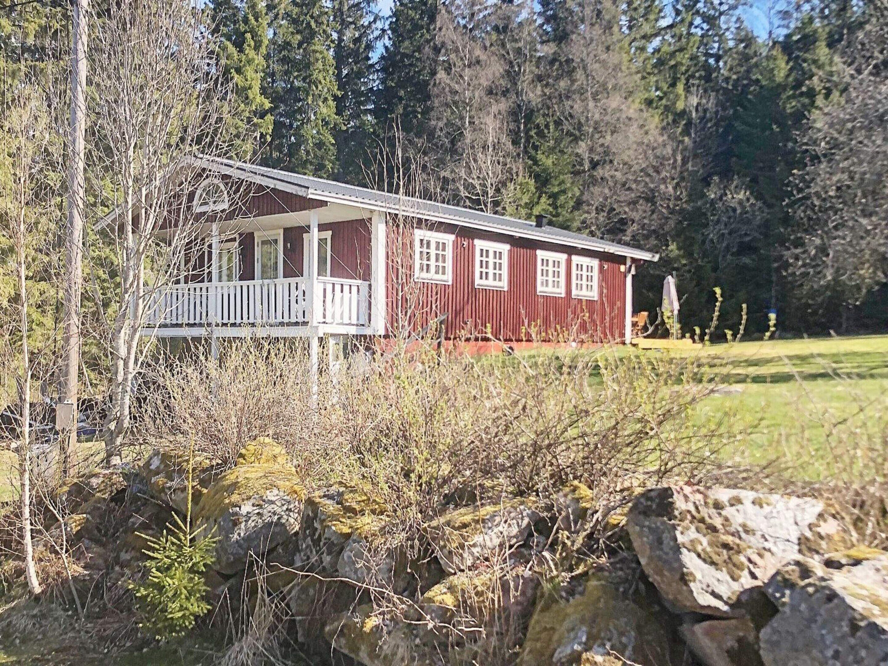 A red cabin with a porch, surrounded by trees and a grassy area.