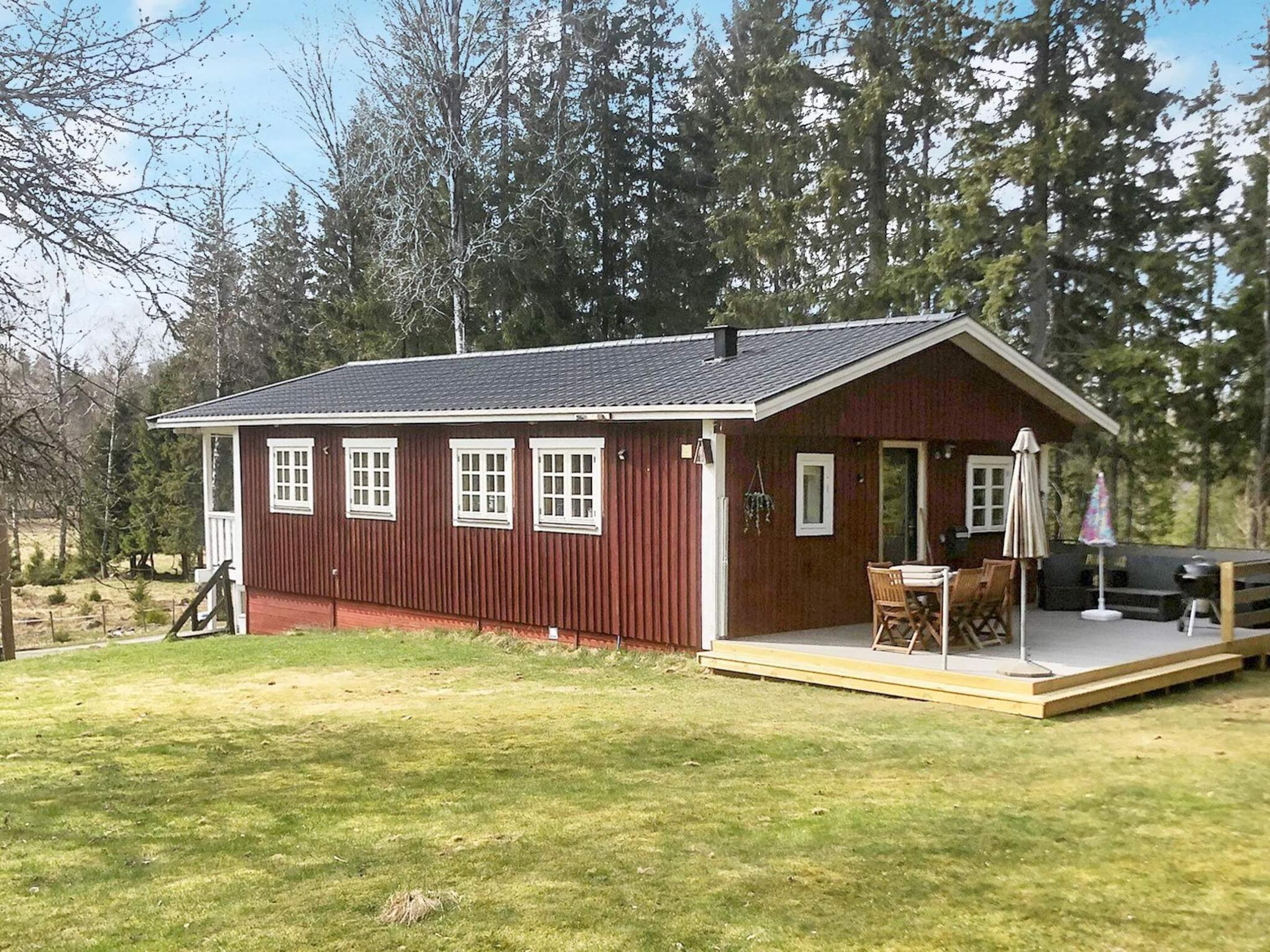 A red wooden cabin with a porch and a table with chairs.