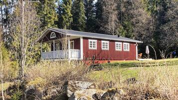 Eine rote Holzhütte mit Veranda, umgeben von Bäumen und einer grünen Wiese.