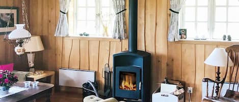 A cozy cabin interior with a wood-burning stove, wooden walls, a dining table, and a rocking chair.