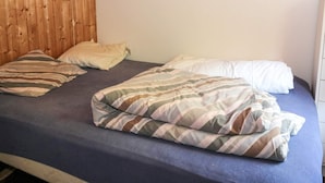 Una cama con ropa de cama a rayas, un cabecero de madera y un objeto rojo en la pared.