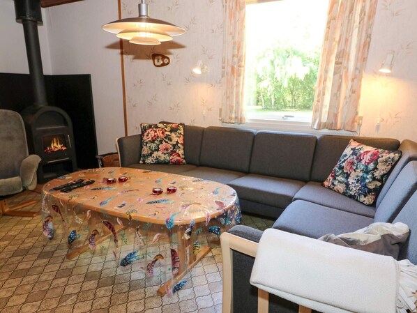A cozy living room with a sofa, a table with decorative items, a fireplace, and a window with curtains. - 6 Person Holiday Home in Hadsund (Hadsund)