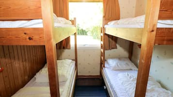 A bunk bed room with wooden frames, a window, and a view of greenery outside.