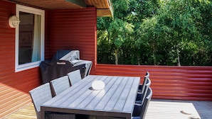 Una terraza de madera con mesa y sillas, una parrilla y una ventana.