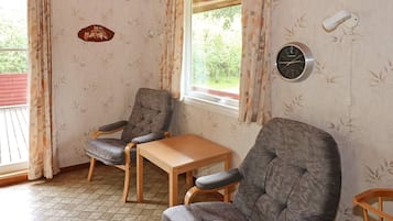 A room with two grey armchairs, a wooden table, a wall clock, and a window with curtains.