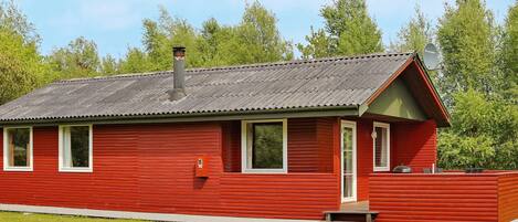 A red wooden cabin with a metal roof, a chimney, and a small porch.