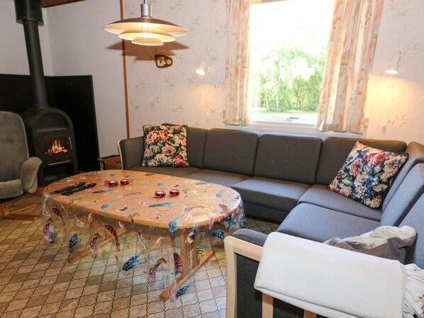 A cozy living room with a sofa, a table with decorative items, a fireplace, and a window with curtains.