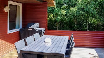 Una terraza de madera con mesa y sillas, una parrilla y una ventana.