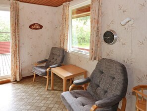 A room with two grey armchairs, a wooden table, a wall clock, and a window with curtains. - 6 Person Holiday Home in Hadsund (Hadsund)