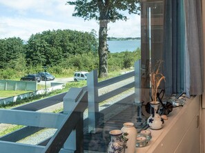 A view from a window overlooking a lake, a wooden deck, and a parking area with cars.