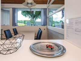 Una habitación moderna con una mesa, sillas, un cuenco decorativo de metal, un coche de juguete y una ventana que ofrece vistas a árboles y una casa.