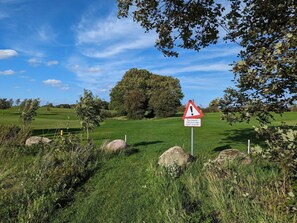 A golf course with a warning sign, trees, and a clear sky. - 6 Person Holiday Home in Aabenraa (Aabenraa)