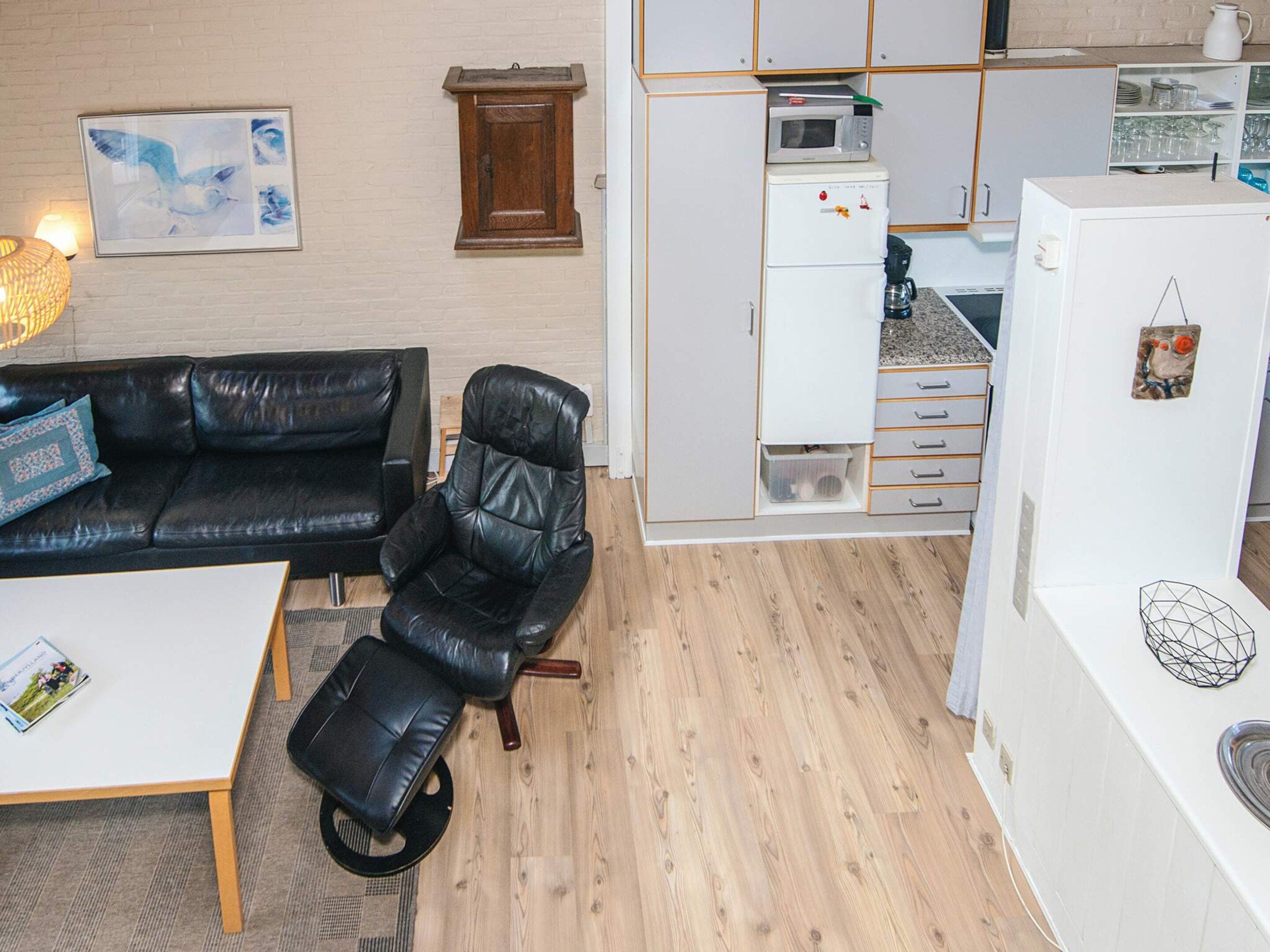 A compact living space with a black leather sofa, a black leather chair, a small coffee table, and a kitchenette area.
