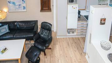Un espacio habitable compacto con sofá y sillón de cuero negro, una mesita de centro pequeña y una zona de kitchenette.