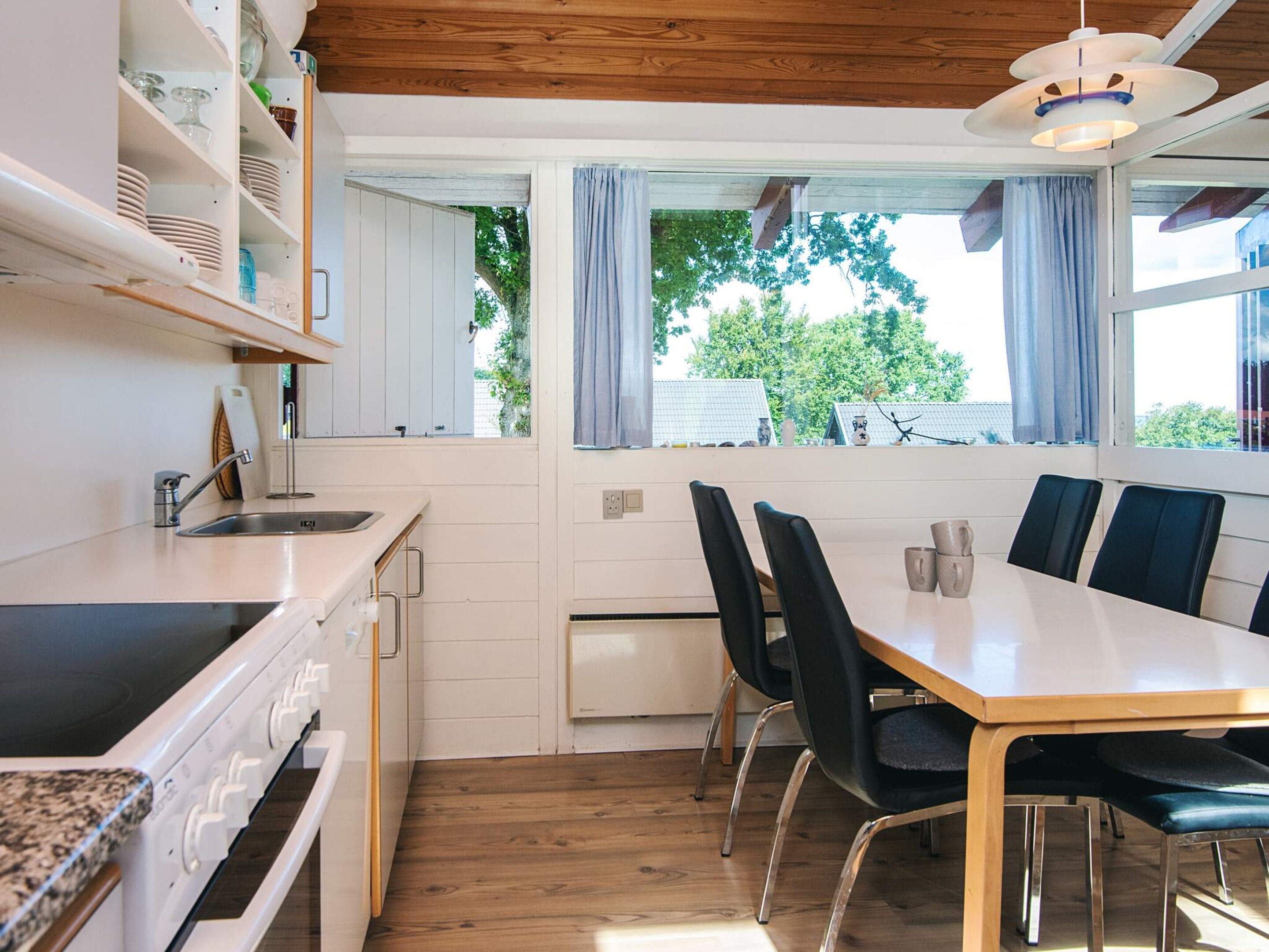 A modern kitchen with a dining area, wooden flooring, and a view of greenery outside.