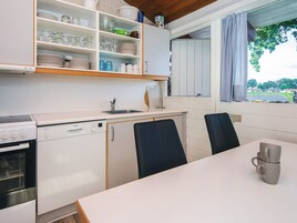 Una cocina compacta con armarios blancos, un lavavajillas Bosch, una estufa y una zona de comedor con dos sillas y una mesa.