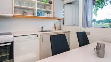Cozinha compacta com armários brancos, máquina de lavar louça Bosch, fogão e área de refeições com duas cadeiras e uma mesa.