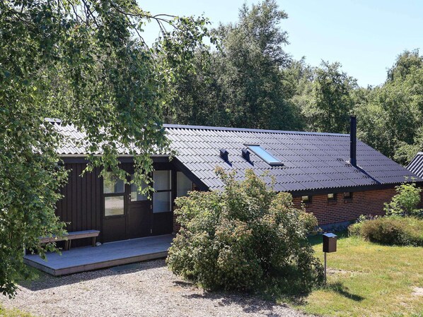 Eine kleine Holzhütte mit geneigtem Dach, einer Veranda und einem Schornstein.