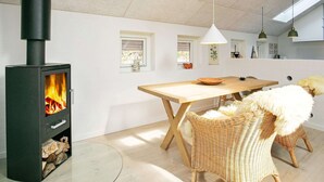 A modern interior with a wood-burning stove, a dining table, wicker chairs, and pendant lighting. - 4 Person Holiday Home in Laeso (Læsø)
