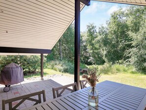 Eine Terrasse im Freien mit Tisch, Stühlen, einem Grill und Blick auf einen bewaldeten Bereich.