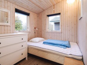 A wooden-paneled room with a bed, a dresser, and two windows.