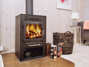 A wood-burning stove with a fire, a wicker basket, and a box of wood.