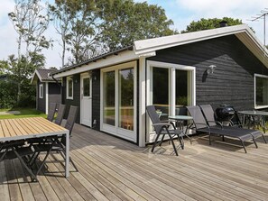 Une terrasse avec une table et des chaises, un barbecue et une porte-fenêtre coulissante donnant sur un espace extérieur abrité.
