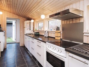 A modern kitchen with wooden paneling, a stainless steel range hood, a built-in oven, and a black countertop.