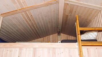 A loft-style room with a wooden slatted ceiling, a bunk bed, and a ladder.