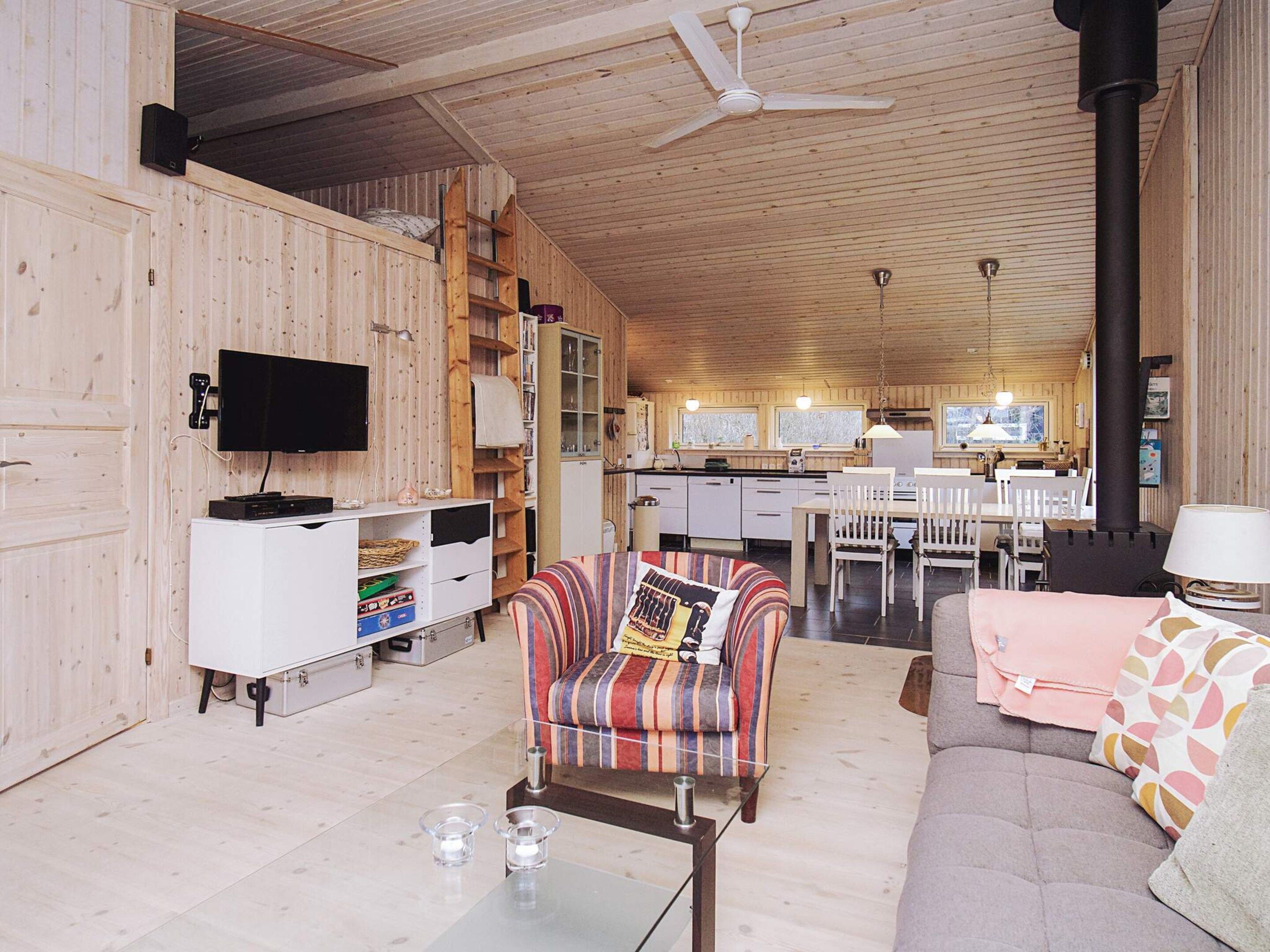 Interior acollidor d'una cabana amb elements de fusta, un sofà, una butaca a ratlles, una taula de dinar i una zona de cuina.
