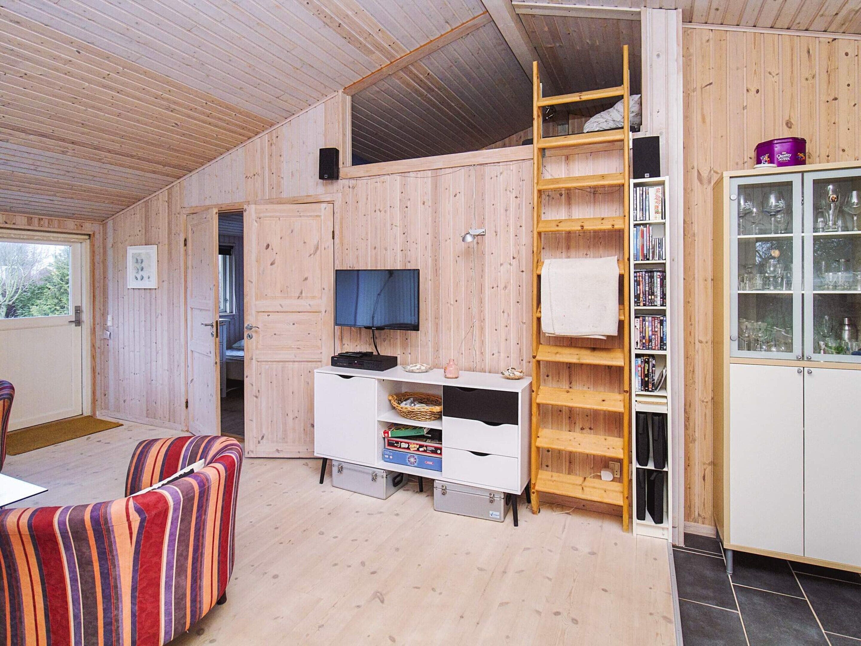 A compact living space with a wooden interior, a television, a bookshelf, and a cabinet with glass doors.