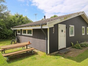 A small cabin with a single door, a window, and a picnic table in the yard.