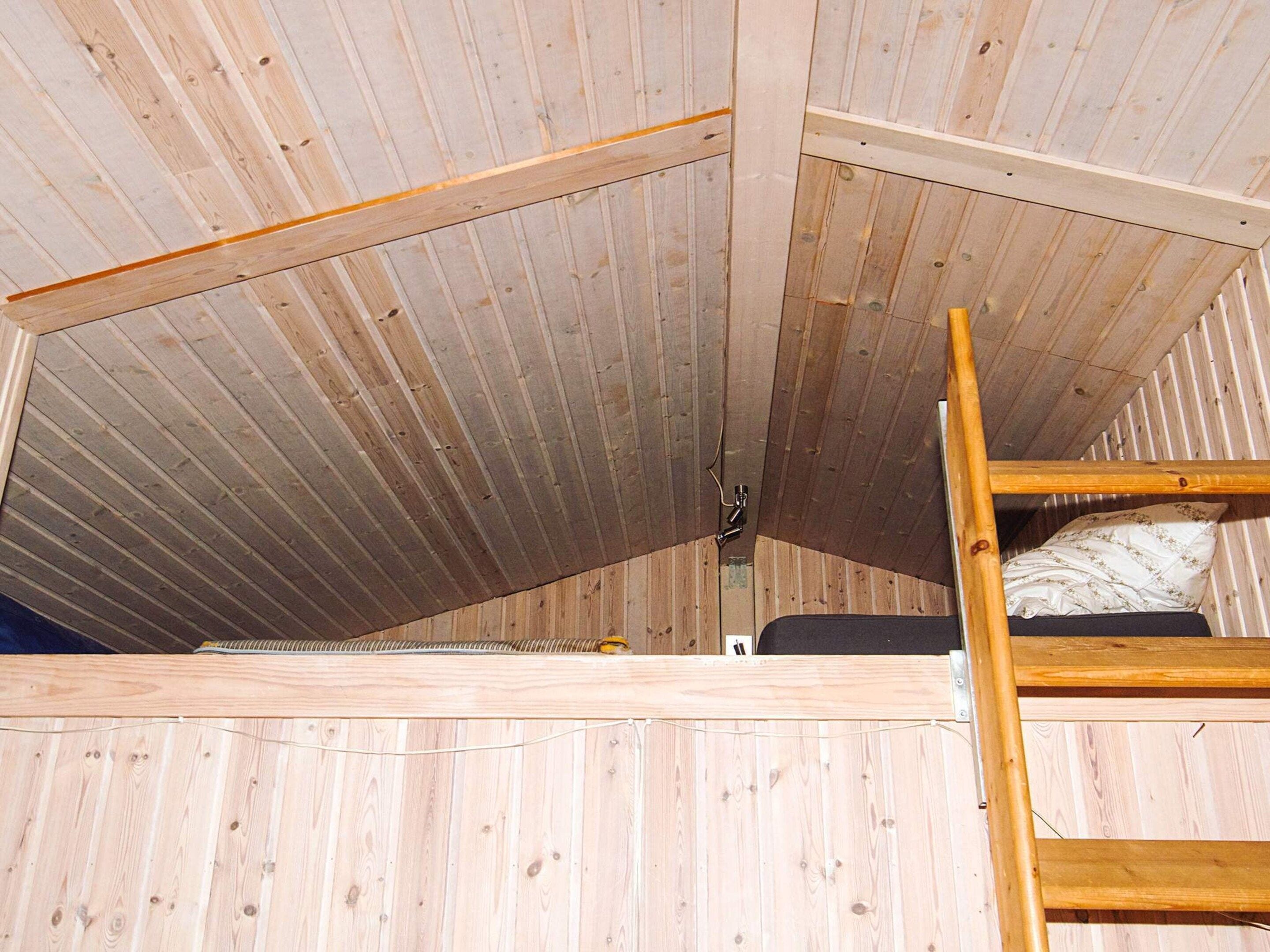 A loft-style room with a wooden slatted ceiling, a bunk bed, and a ladder.