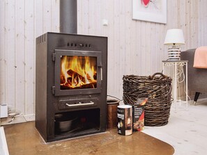 A wood-burning stove with a fire, a wicker basket, and two cans of wood pellets on the floor. - 6 Person Holiday Home in Slagelse (Slagelse)