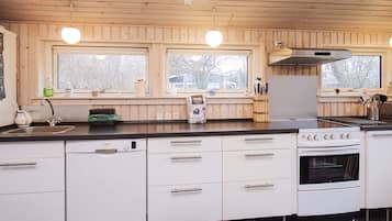 A kitchen with wooden cabinets, a Bosch dishwasher, a stove, and two windows with a view of trees.