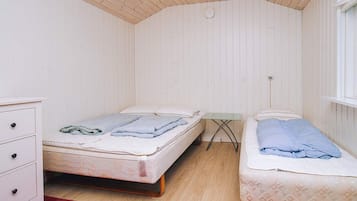 A room with two beds, a small table, a dresser, and a red rug.