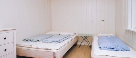 A room with two beds, a small table, a dresser, and a red rug.