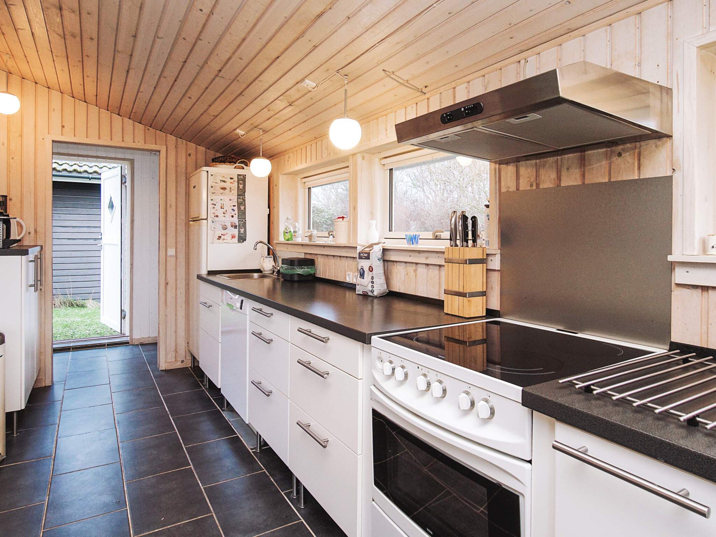 A modern kitchen with white cabinets, a stainless steel range hood, and a black countertop.