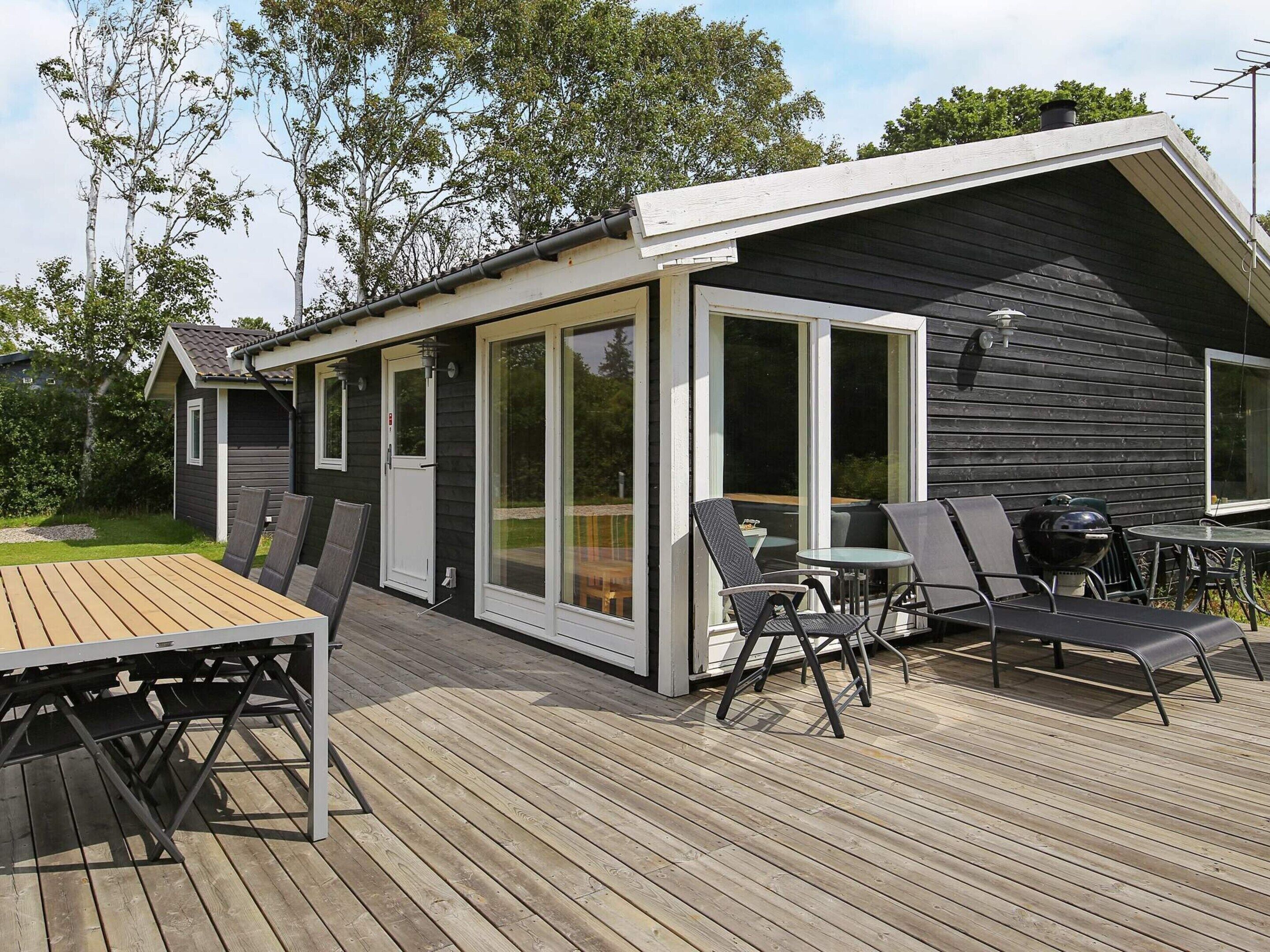 A deck with a table and chairs, a grill, and a sliding glass door leading to a covered outdoor area.