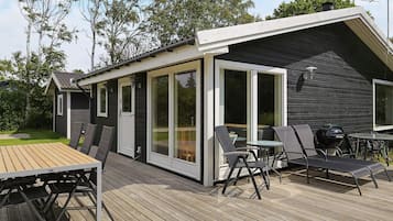 A deck with a table and chairs, a grill, and a sliding glass door leading to a covered outdoor area.