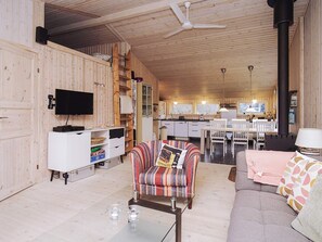 A cozy cabin interior with a wooden interior, a sofa, a striped armchair, a dining table, and a kitchen area.