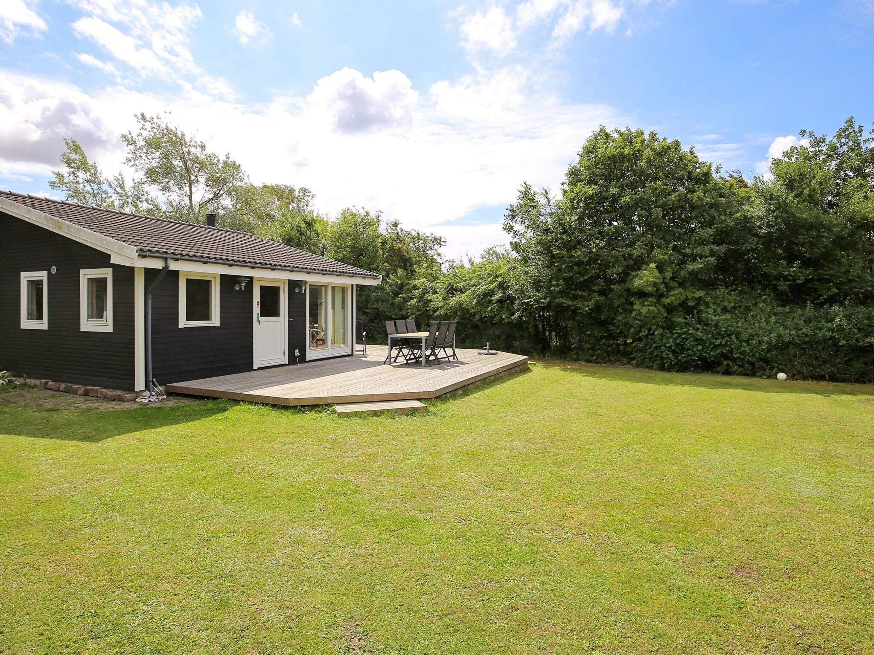 A single-story house with a deck, a patio with outdoor furniture, and a well-maintained lawn.