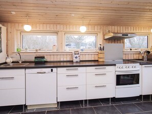 A modern kitchen with white cabinets, a Bosch dishwasher, a stove, and a window with a view of trees. - 6 Person Holiday Home in Slagelse (Slagelse)