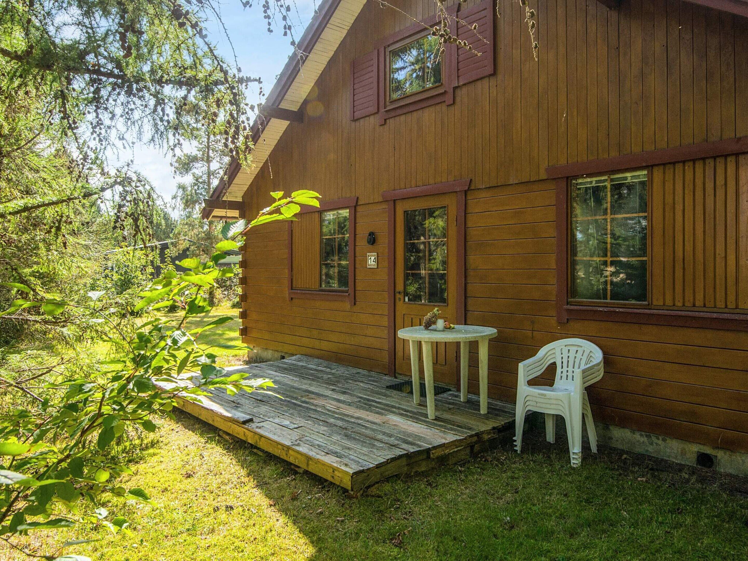 A wooden cabin with a deck, a small table, and a chair.