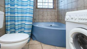 A bathroom with a toilet, a blue bathtub, and a washing machine.