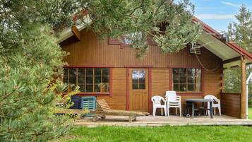 A wooden cabin with a porch, a table, and chairs.