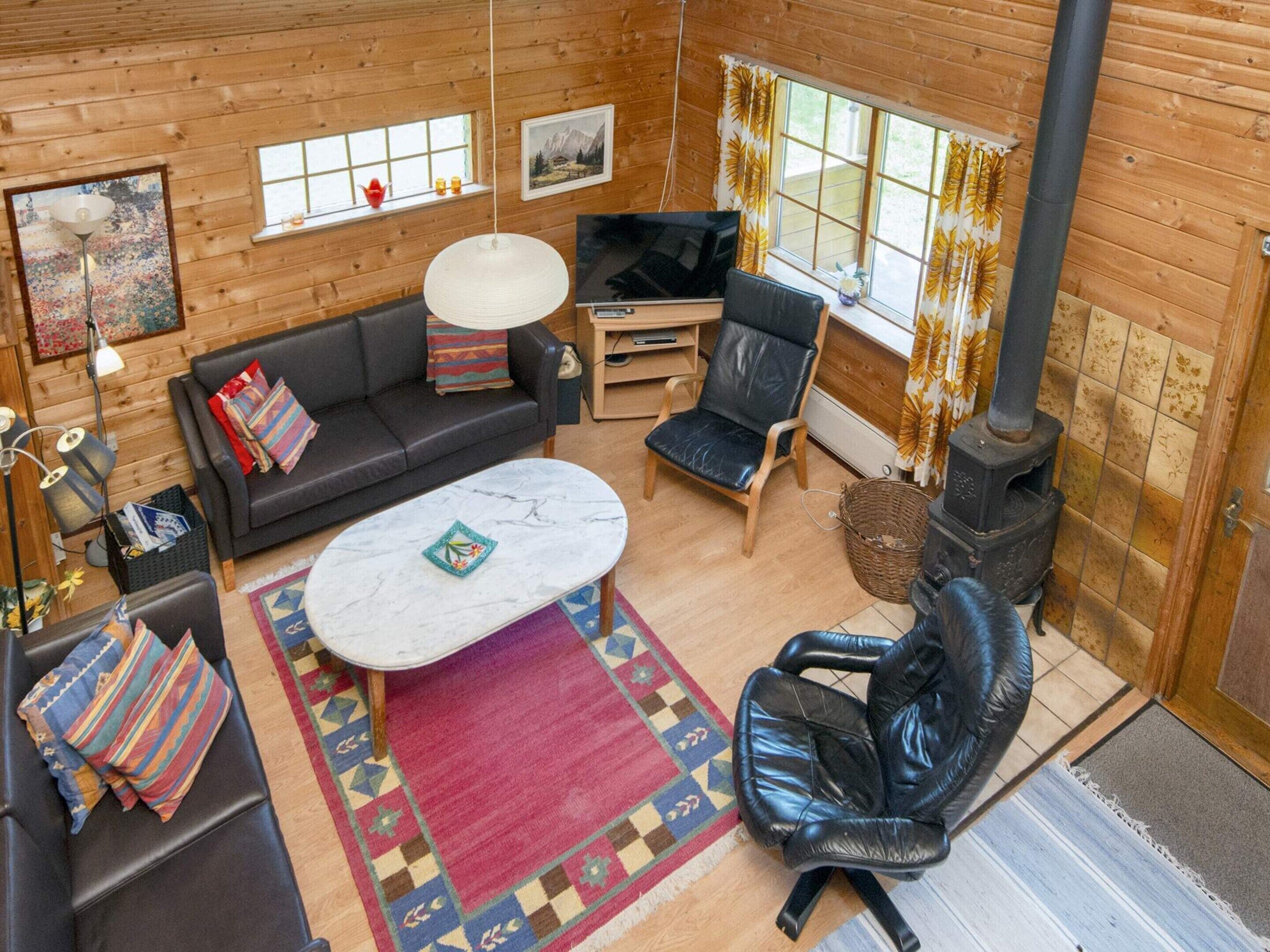 A cozy cabin interior with a sofa, armchair, television, and a fireplace.